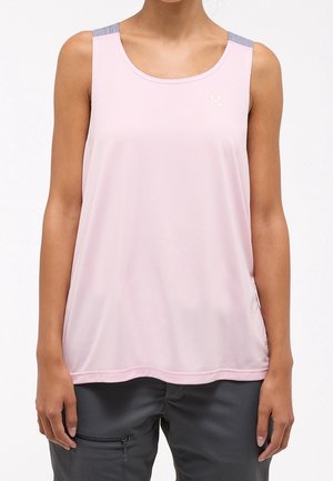 Nainen, jolla on vaaleanpunainen hihaton urheilutoppi ja tummanharmaat housut, joissa on vetoketjullinen tasku. Kuvassa näkyvät hänen hartiansa vyötäröön saakka.