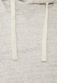 Hoodie gris clair en tissu texturé, avec un décolleté en V et des cordons de serrage de couleur crème. Motif subtil de taches tout au long.