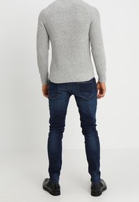 Grauer gerippter Strickpullover, schmal geschnittene dunkelblaue Jeans, schwarze Schuhe. Ansicht von hinten, die Textur und Passform hervorhebend. Einfaches Design, ohne Muster.