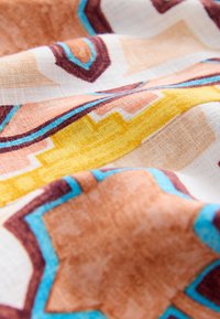 Tissu présentant un motif géométrique avec des accents marron, jaune et bleu sur un fond crème ; texture lisse avec une sensation douce et tissée.