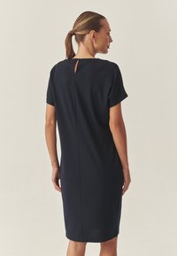 Marineblaues, knielanges Kleid mit kurzen Ärmeln, Details im Schlüssel-Ausschnitt hinten und gerader Schnitt, gefertigt aus einem glatten, weich anfühlenden Stoff.
