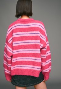 Přehozený svetr s velkými růžovými a červenými pruhy s fialovými akcenty, vyrobený z chlupatého materiálu; má spuštěná ramena a žebrovaný výstřih.