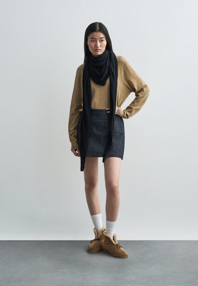 Pruun kudumisae, tume denim mini-seelik, must sall, valged põlvikud ja pruunid sussid karvase äärega. Minimalistlik taust.