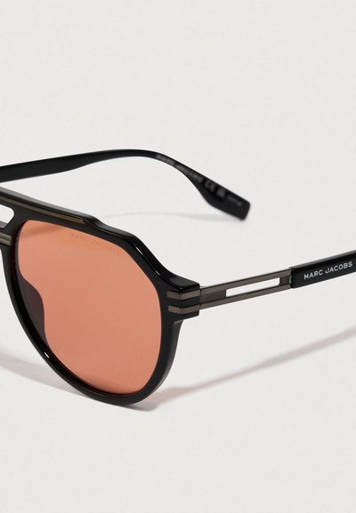 Zwarte Marc Jacobs zonnebril met oranje getinte ronde lenzen en slanke metalen armen op een witte achtergrond.