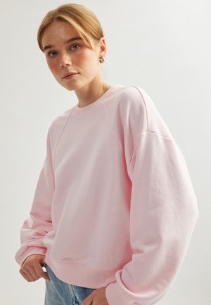 Sweatshirt rosa con scollo a girocollo, maniche raglan e polsini a costine. Il tessuto appare morbido e strutturato, adatto per un abbigliamento casual.