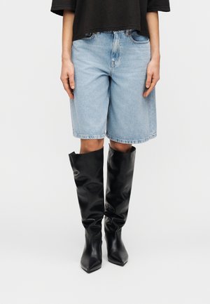 Denim shorts in light blue, featuring a relaxed fit, cuffed hems, paired with knee-high black leather boots with a pointed toe design.