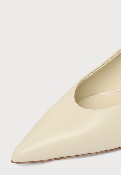 Gros plan d'une chaussure en cuir couleur crème à bout pointu avec une texture lisse et une ouverture basse.
