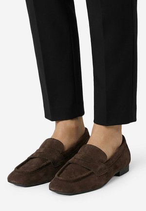 Braune Wildleder-Loafer, getragen zu schwarzen, gekürzten Hosen, an nackten Füßen gestylt, zeigen einen klassischen und minimalistischen Look.