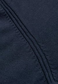 Tissu bleu marine avec une texture tricotée fine, présentant des coutures visibles le long des bords et un léger éclat.