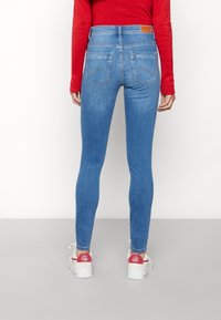 Jeans ajustados azules de mezclilla, con una cintura de altura media, bolsillos traseros con acentos de costura y una silueta entallada, combinados con zapatillas blancas.