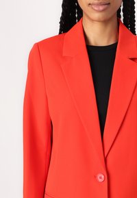 Rode blazer met een notch-lapel, enkele knoopsluiting en gestructureerde mouwen, vervaardigd uit een gladde stof met een getailleerde pasvorm.