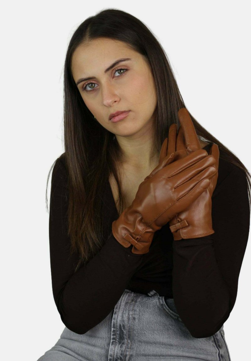 Brązowe skórzane rękawiczki o gładkiej fakturze i przeszyciach, dopasowane do dłoni z akcentami na kostkach, trzymane przez osobę.