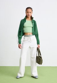 Veste zippée verte avec un accent blanc, crop top côtelé vert clair, pantalon baggy blanc et baskets argentées. Sac à main vert olive inclus.