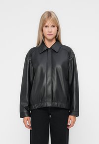 Veste en simili cuir noir avec un col, fermeture éclair, ourlet élastique et coupe légèrement oversize. Texture lisse et design décontracté.