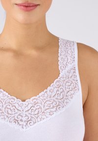 Witte camisole met een v-halsontwerp, voorzien van delicate kantafwerking bij de kraag. Soepele stof met geen extra patronen of accenten.