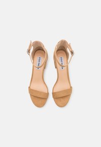 Tan mockaskärpade sandaler med klackar som har vristremmar, breda tår och mittfotsband, samt en mjuk fusk läder innersula. Justerbara spännen ingår.