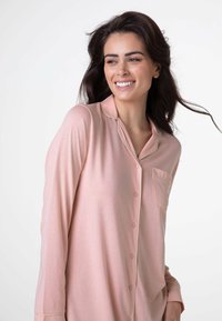 Pigiama a maniche lunghe, rosa chiaro, realizzato in tessuto morbido, con apertura frontale a bottoni, colletto, tasca e piping a contrasto lungo il colletto.
