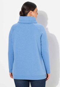 Maglione blu chiaro con colletto alto, maniche raglan e polsini a coste. Texture morbida e vestibilità comoda, abbinato a jeans scuri.