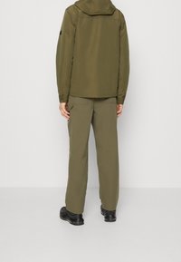 Chaqueta verde oliva con capucha y ligero brillo, combinada con pantalones verde oliva a juego. El atuendo presenta un corte entallado y bolsillos utilitarios.