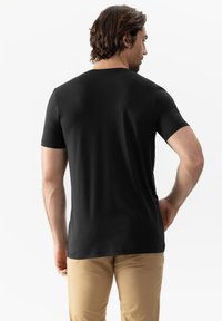 Černé tričko s krátkým rukávem vyrobené z měkké tkaniny, s kulatým výstřihem a hladkým povrchem, z pohledu zezadu s khaki kalhotami.