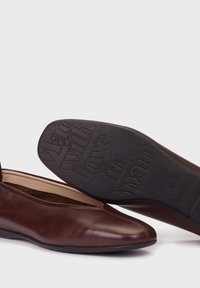 Burgundy leather flat shoes with a rounded toe and an elastic band. Black rubber sole features embossed text: “Made with love in Spain.”