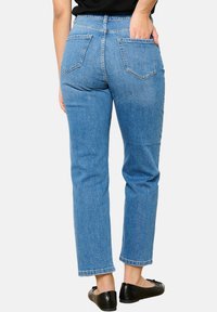Jeans de tiro alto en un azul claro, con corte recto, que incluyen dos bolsillos traseros y un ligero efecto de deslavado. Textura de denim suave y puños rematados.