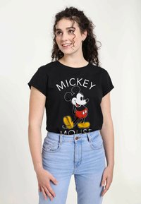 Černé bavlněné tričko s předním potiskem Mickey Mouse, s bílým textem "MICKEY" nad a "MOUSE" pod ním v tučném písmu.