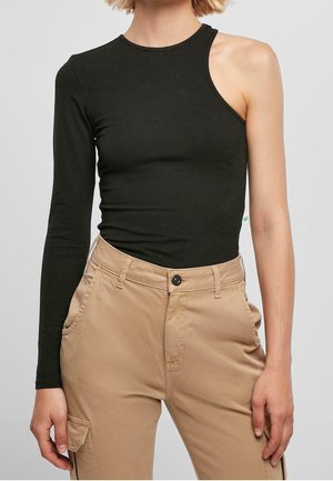 Person trägt ein schwarzes asymmetrisches Langarmoberteil mit einer freiliegenden Schulter und beige hochtaillierte Cargo-Hosen.