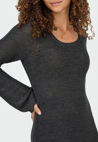 Pull en tricot gris foncé avec un col arrondi, tissu texturé, manches longues et silhouette ajustée, doté de détails en maille ouverte.