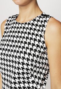 Mustat ja valkoiset houndstooth-kuvioidut hihattomat topit, joissa on sileä kangas ja olkaimet.