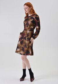 Een bruin en bordeauxrood dress met een ronde hals, lange mouwen en een uitlopende rok, met een spattenpatroon en een taille die is aangesnoerd.