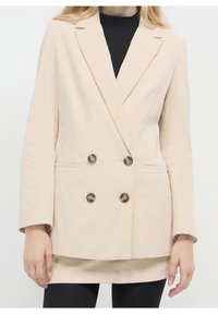 Beżowa żakietowa marynarka z prążkowanego sztruksu, dwurzędowa, z klapami z wycięciami, dużymi ciemnymi guzikami i pionową prążkowaną teksturą. Posiada boczne kieszenie.
