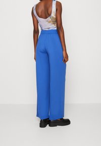 Blå vida byxor med elastisk midja, kombinerat med en ärmlös topp med ett lätt mönster. Slät textur och löst sittande.