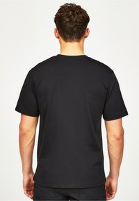 Musta puuvillainen T-paita lyhyillä hihoilla, pyöreällä kaula-aukolla ja yksinkertaisella selkädesignilla. Kangas on sileä ja siinä on slim fit -leikkaus. Ei näkyviä kuvioita tai koristeita.