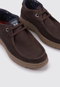 Chaussures en cuir marron avec des bouts ronds, détails cousus et semelles en caoutchouc. L'intérieur présente une doublure en tissu à motif.