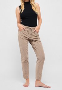 Turkosa manchesterbyxor med resårmidja, snörning och sidofickor, i kombination med en åtsittande svart ärmlös topp.