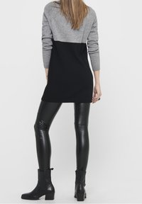 Abito maglione grigio e nero abbinato a leggings in pelle nera lucida e stivaletti con tacco a blocco.