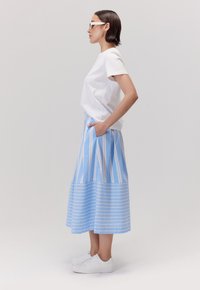 Biała koszula z krótkim rękawem zestawiona z niebieską i białą spódnicą w paski z kieszeniami, uzupełniona białymi sneakersami i okularami przeciwsłonecznymi.