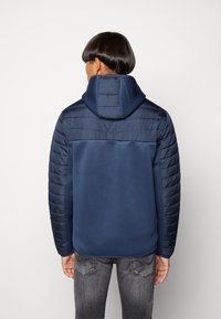 Marineblauwe hoodie met een gladde body en gevoerde, gewatteerde mouwen. De stof lijkt zacht met een gestructureerde kraag en een capuchon.