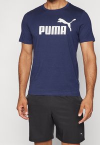 Camiseta de manga corta azul marino hecha de tela suave, que presenta un gran logo blanco de "PUMA" y un gráfico de un gato saltando en el pecho.