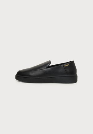 Chaussure noire en cuir à enfiler avec une semelle épaisse et un petit logo doré "HUGO" sur le côté du talon.