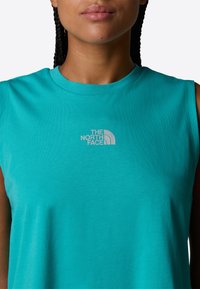 Turquoise mouwloos t-shirt van zacht stof; beschikt over een klein grijs logo van "The North Face" op het borstgebied.