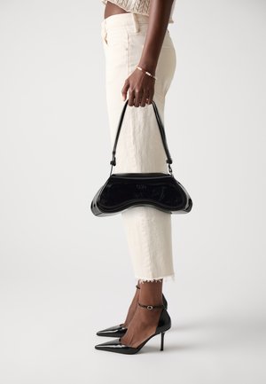 Black patent leather handbag with a curved shape and top handle, worn with cream-colored jeans and black pointed toe heels.