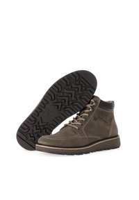 Braune Wildleder-Stiefeletten mit runder Zehenform, ausgestattet mit Metallösen, beigen Schnürsenkeln und einer strukturierten schwarzen Gummisohle mit geometrischem Muster.