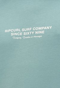 Tricou din bumbac de culoare teal deschis, cu text alb care spune "Ripcurl Surf Company Since Sixty Nine" și detalii de locație în partea de jos.