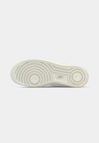 Sola de sneaker branca em borracha com ranhuras circulares, aderência texturizada e logotipo em relevo. Superfície lisa com um design de calcanhar arredondado.