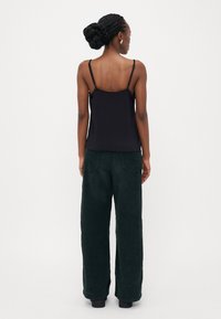 Zwarte spaghetti-top gecombineerd met wijde donkergroene corduroy broek met achterzakken. Soepele textuur en relaxed fit.