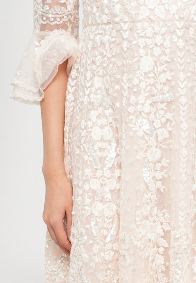Kanten jurk in zachte blush met bloem borduursels, pailletten en belmouwen. Heeft een gestructureerde stof en ingewikkelde details.