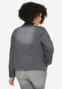 Veste en denim gris foncé avec un col classique, des manches longues et des poches, présentant une texture légèrement décolorée et des accents de boutons.