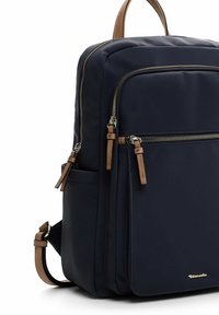 Tumši zila auduma mugursoma ar ādas akcentiem, divām šķērsojošām kabatām un regulējamu siksnu. Virsma gluda ar delikātu spīdumu.